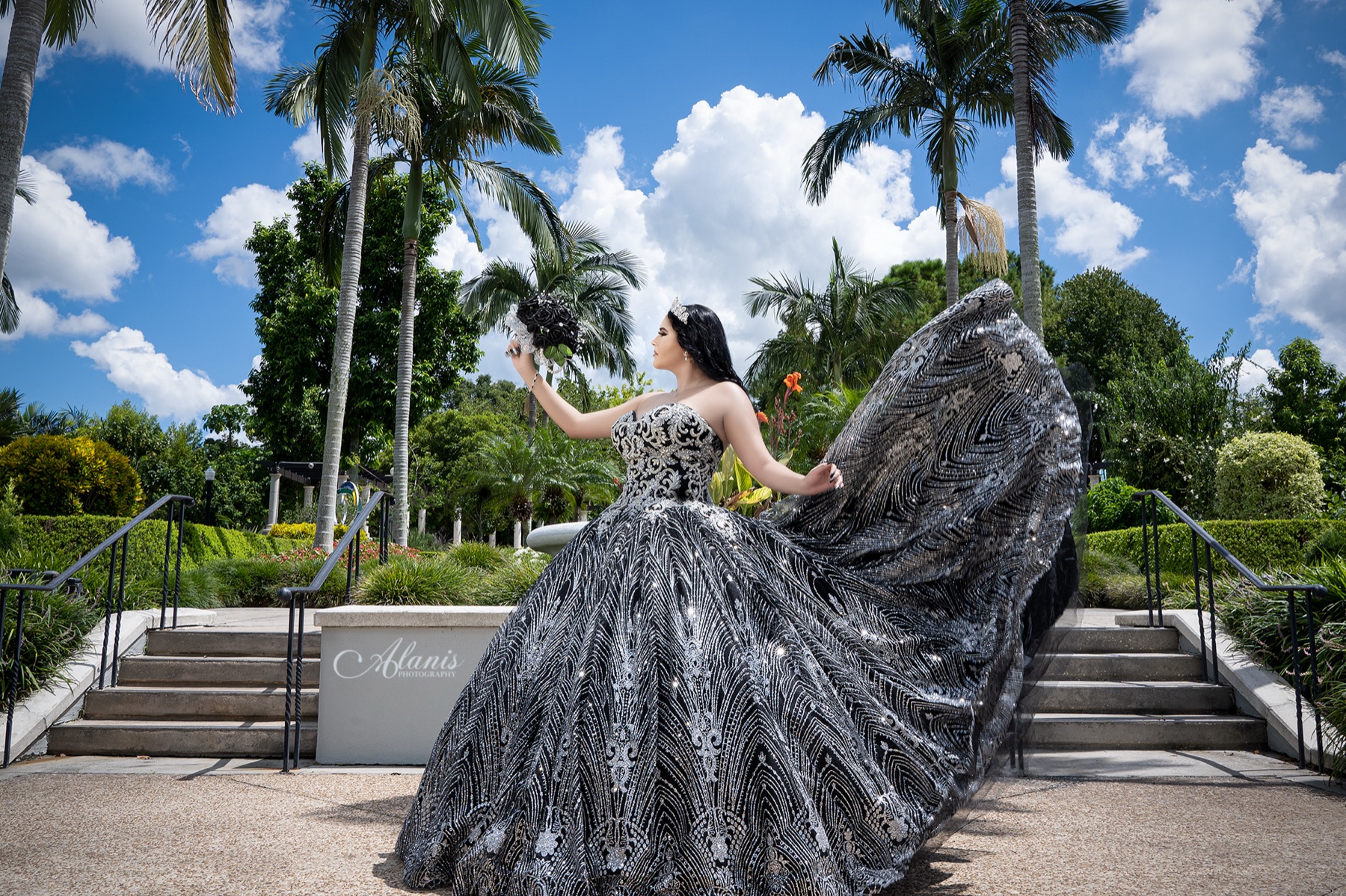 Quinceañera in a sparkling black and silver gown beneath palm trees