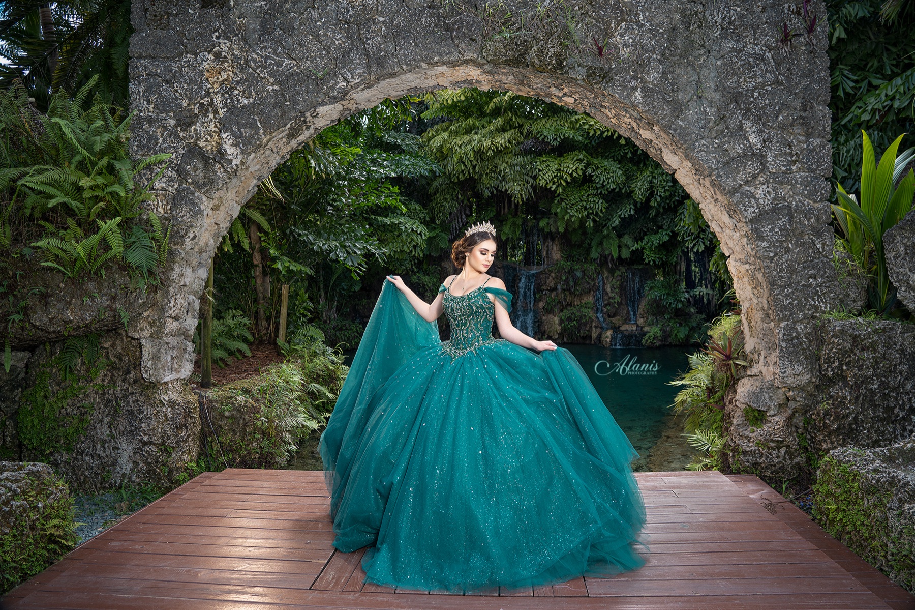 Quinceañera in a teal gown framed by a historic stone arch