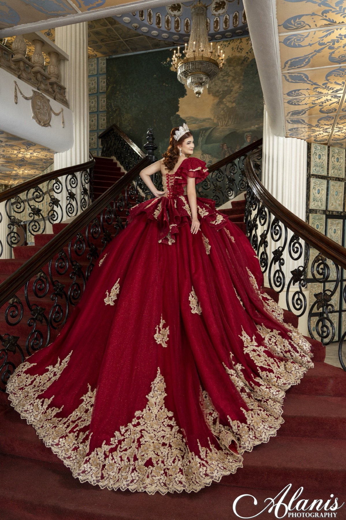 Quinceañera in a red gown on an ornate staircase