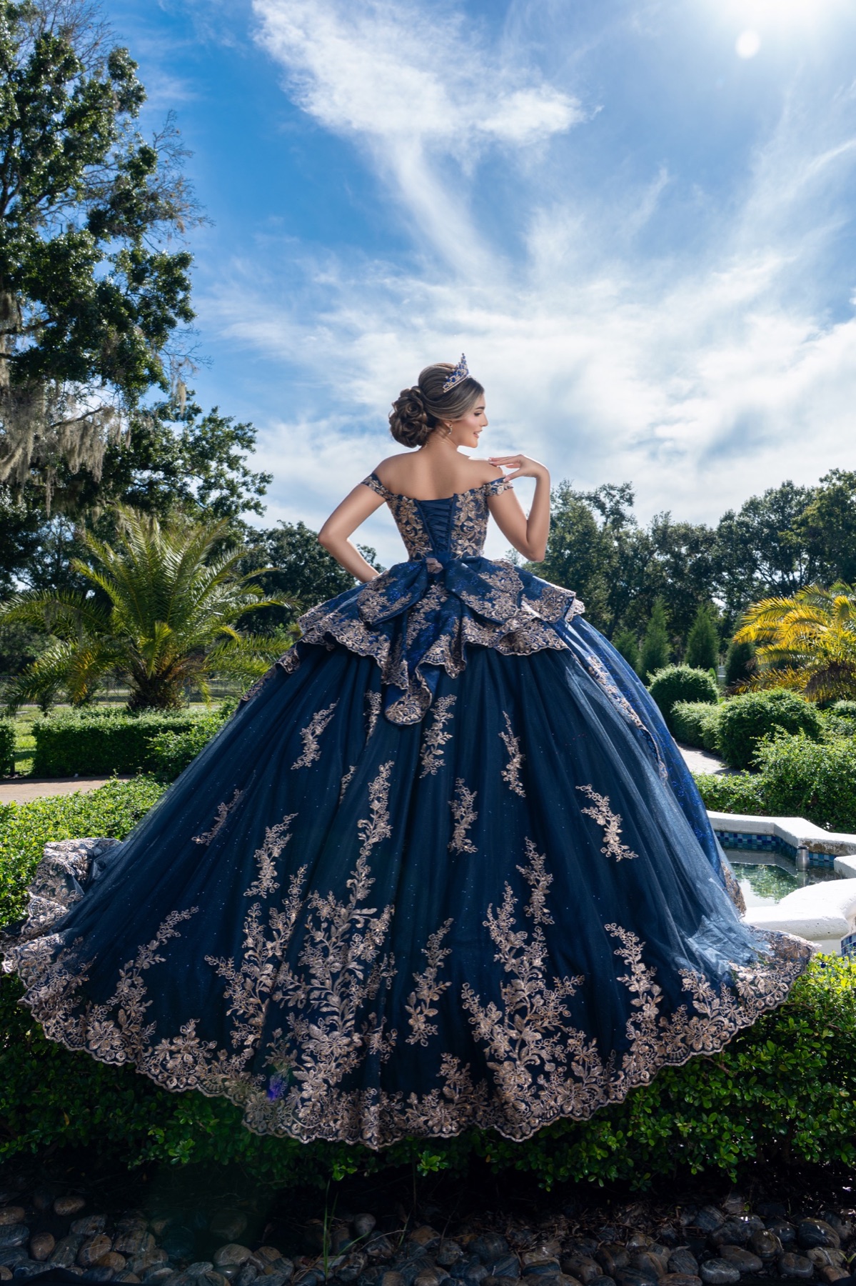 Quinceañera showing the back of a blue embroidered gown in a garden