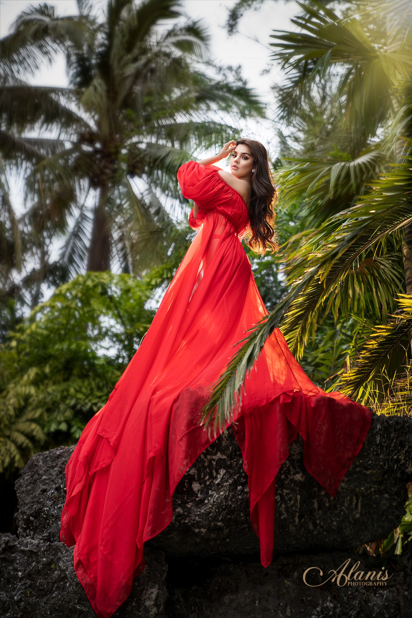 Quinceañera in a red gown among tropical palms