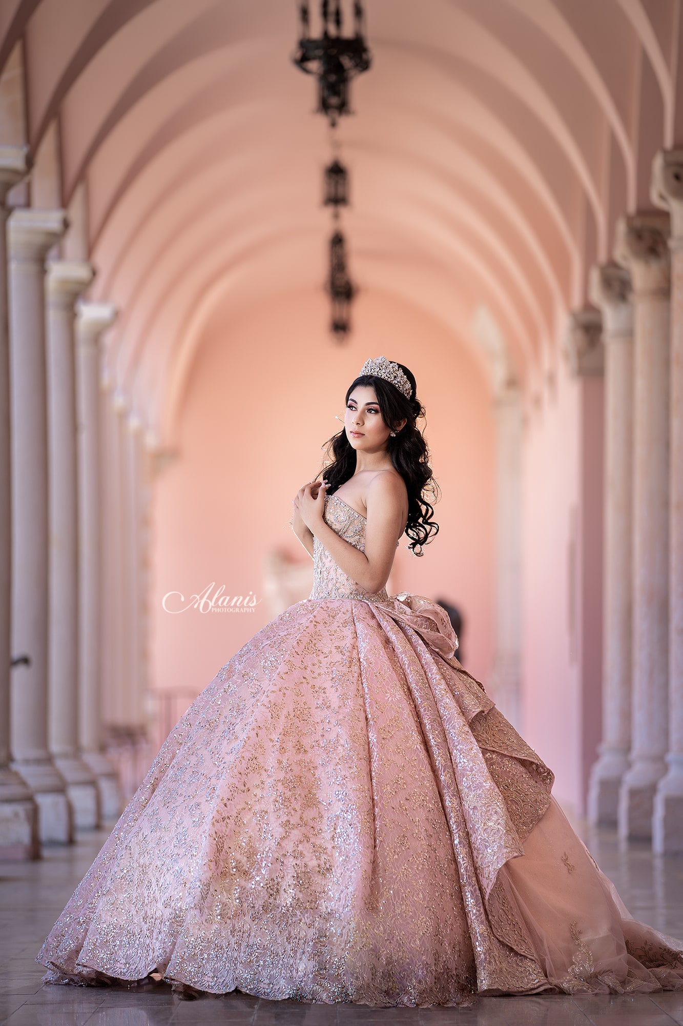 Quinceañera in a blush gown beneath graceful arches