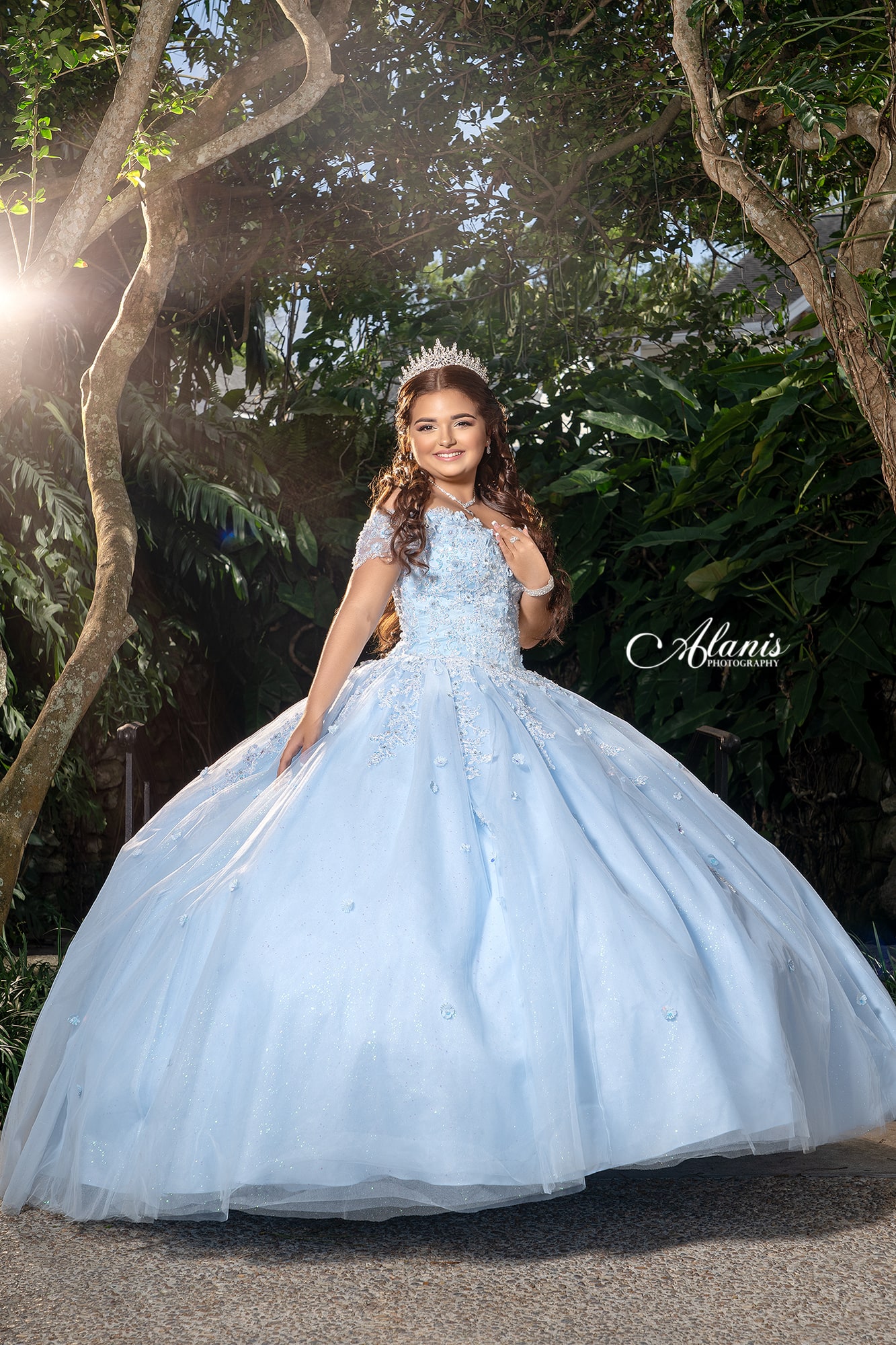 Quinceañera in a pale blue gown beneath a tree