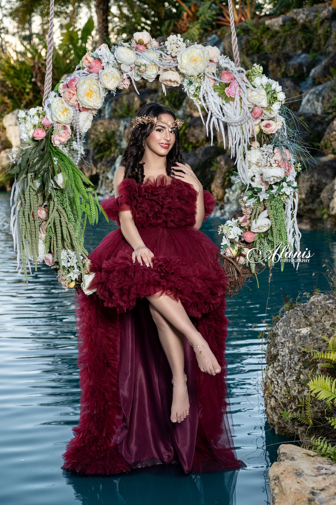 Quinceañera in a burgundy gown on a floral swing