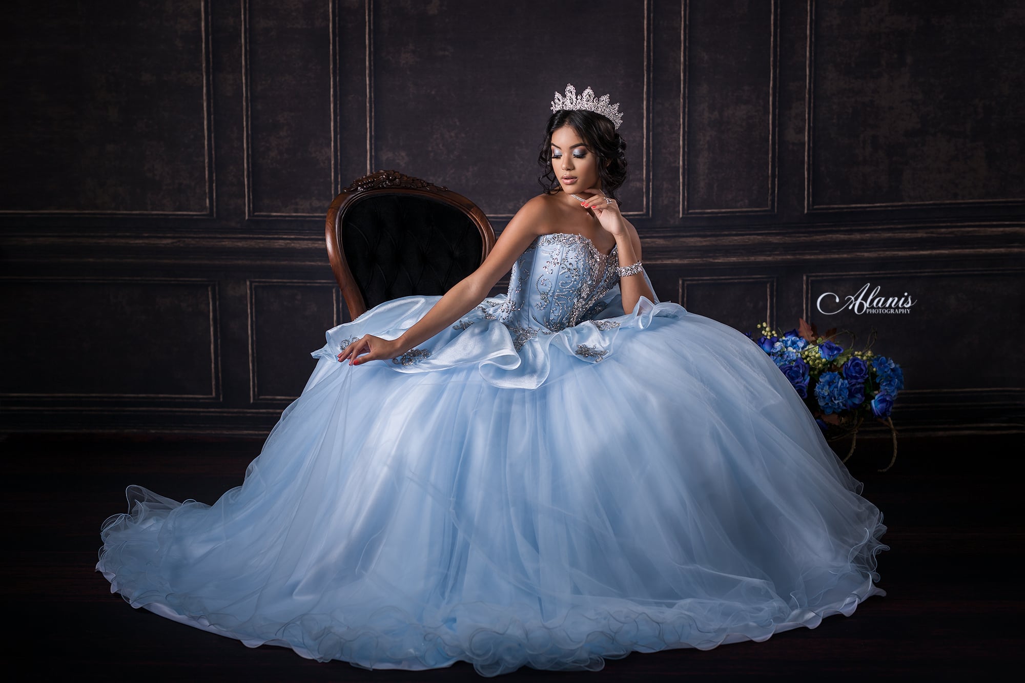 Quinceañera in a pale blue gown seated in a studio